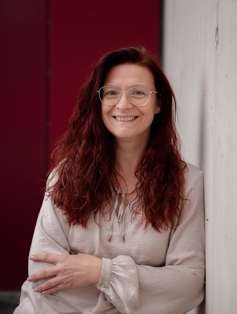 Tanja Wünsch lehnt lächelnd an einer Betonwand – Gesundheitspraktikerin für Männer mit Prostata Probleme Bayreuth