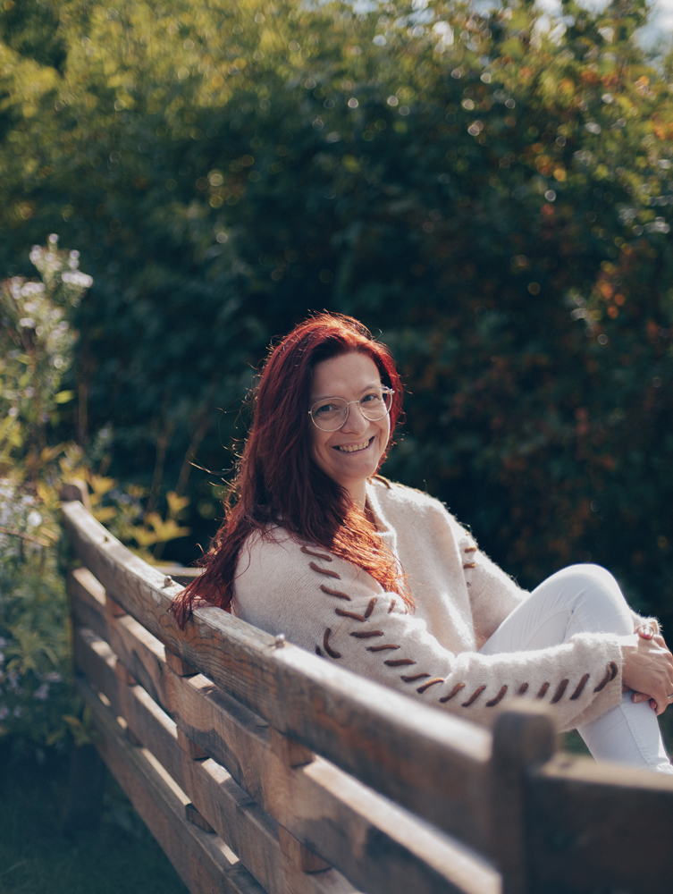 Tanja Wünsch sitzt lachend auf einer Bank im Sonnenschein. Sie bietet Männergesundheit in Bayreuth an