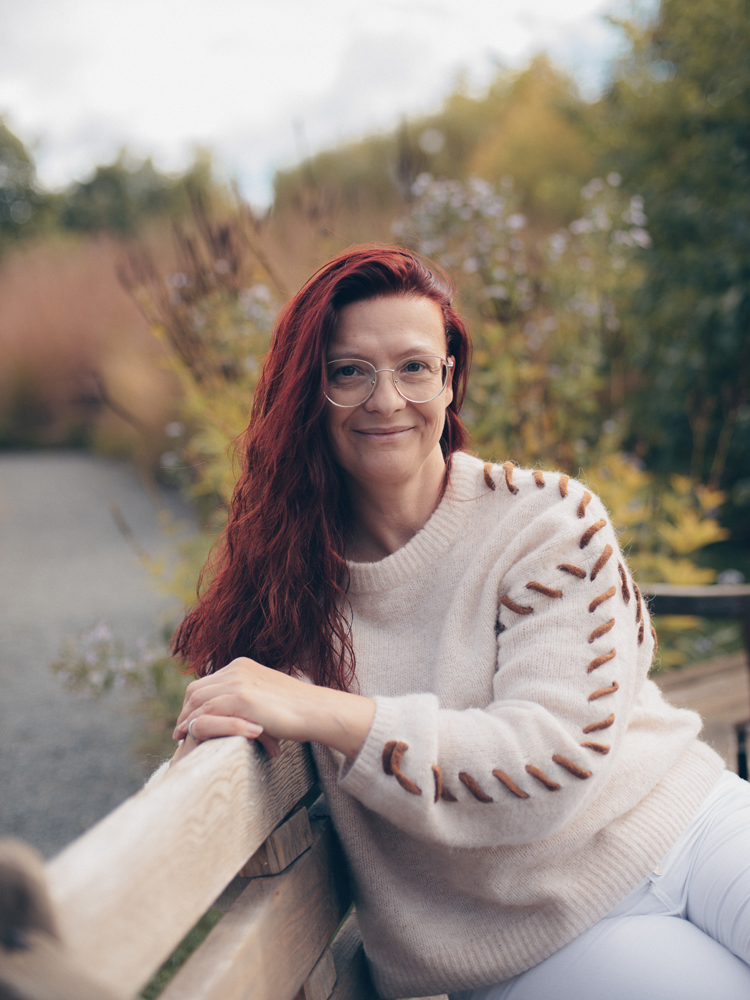 Tanja Wünsch sitzt in der Natur auf einer Parkbank. Sie bietet Prostatahilfe in Bayreuth an.